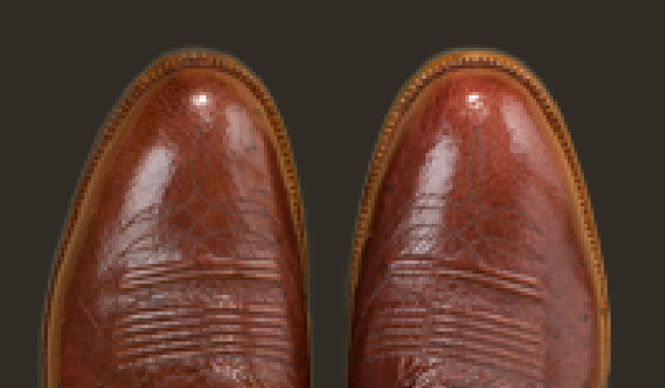 A pair of custom handmade cowboy boots with visible stitching and a shiny, polished finish on a dark background.
