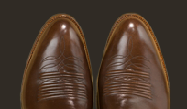 Close-up view of a pair of brown leather custom handmade cowboy boots showcasing decorative stitching on the toe area.