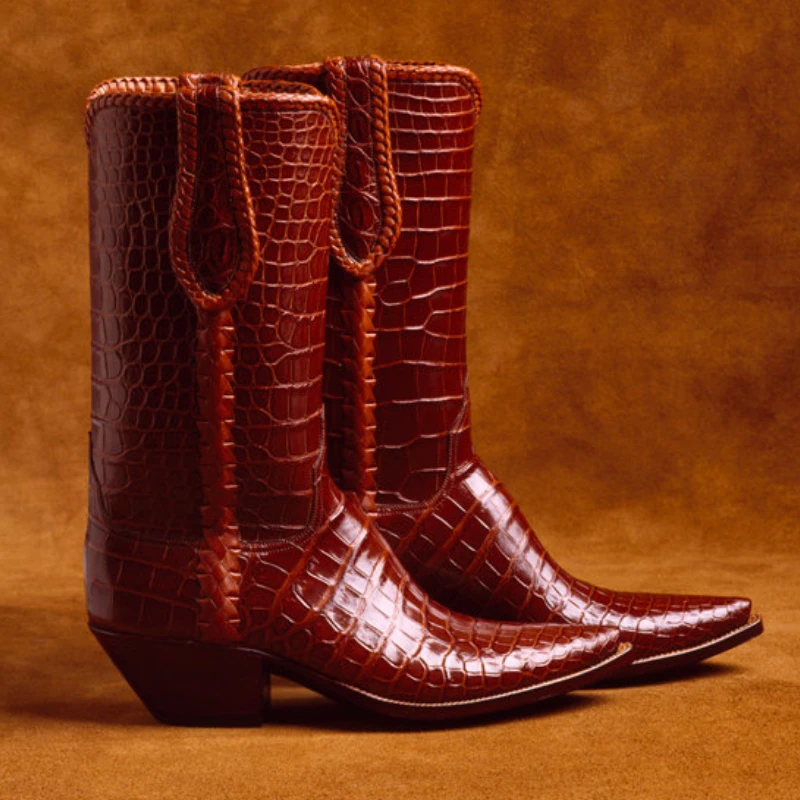 A pair of brown, crocodile-pattern cowboy boots with pointed toes and mid-height heels, placed against a matching brown background.