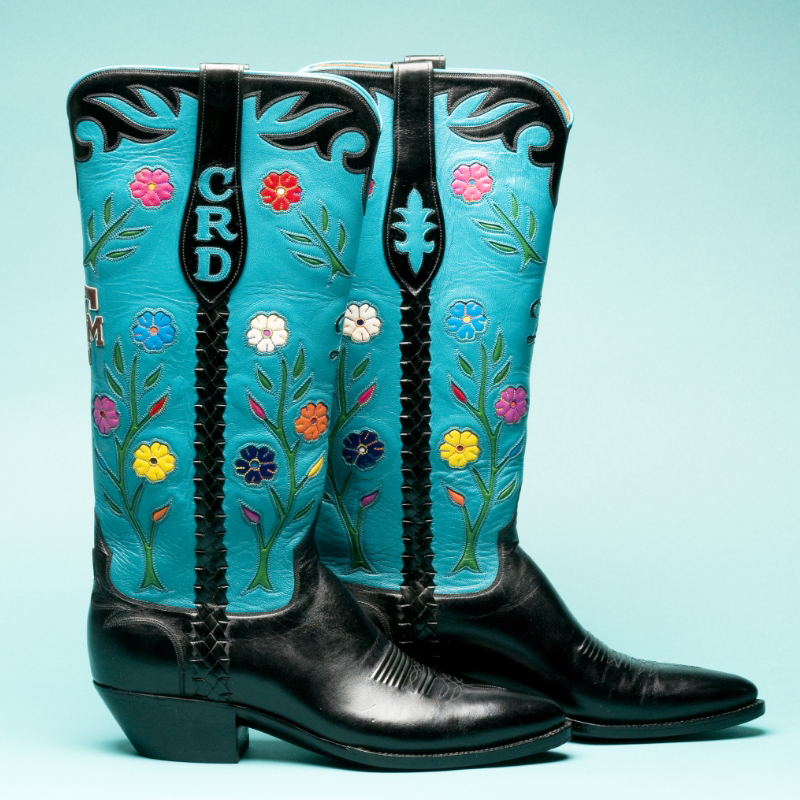 Pair of black leather cowboy boots with light blue upper sections featuring multicolored floral embroidery and the initials "CRD."