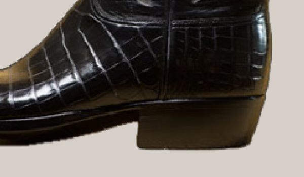 Close-up of the heel of a black, crocodile-patterned leather boot.