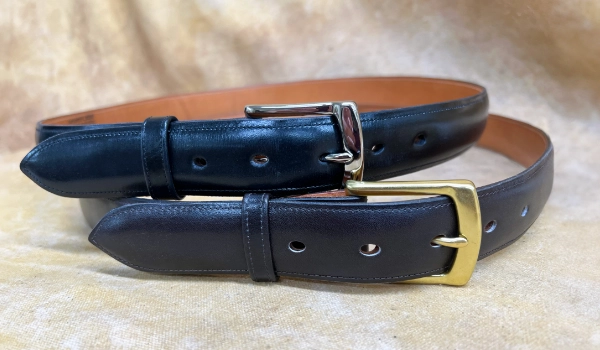 A black leather belt with a silver buckle is shown on top of a brown leather belt with a gold buckle, both resting on a beige surface.