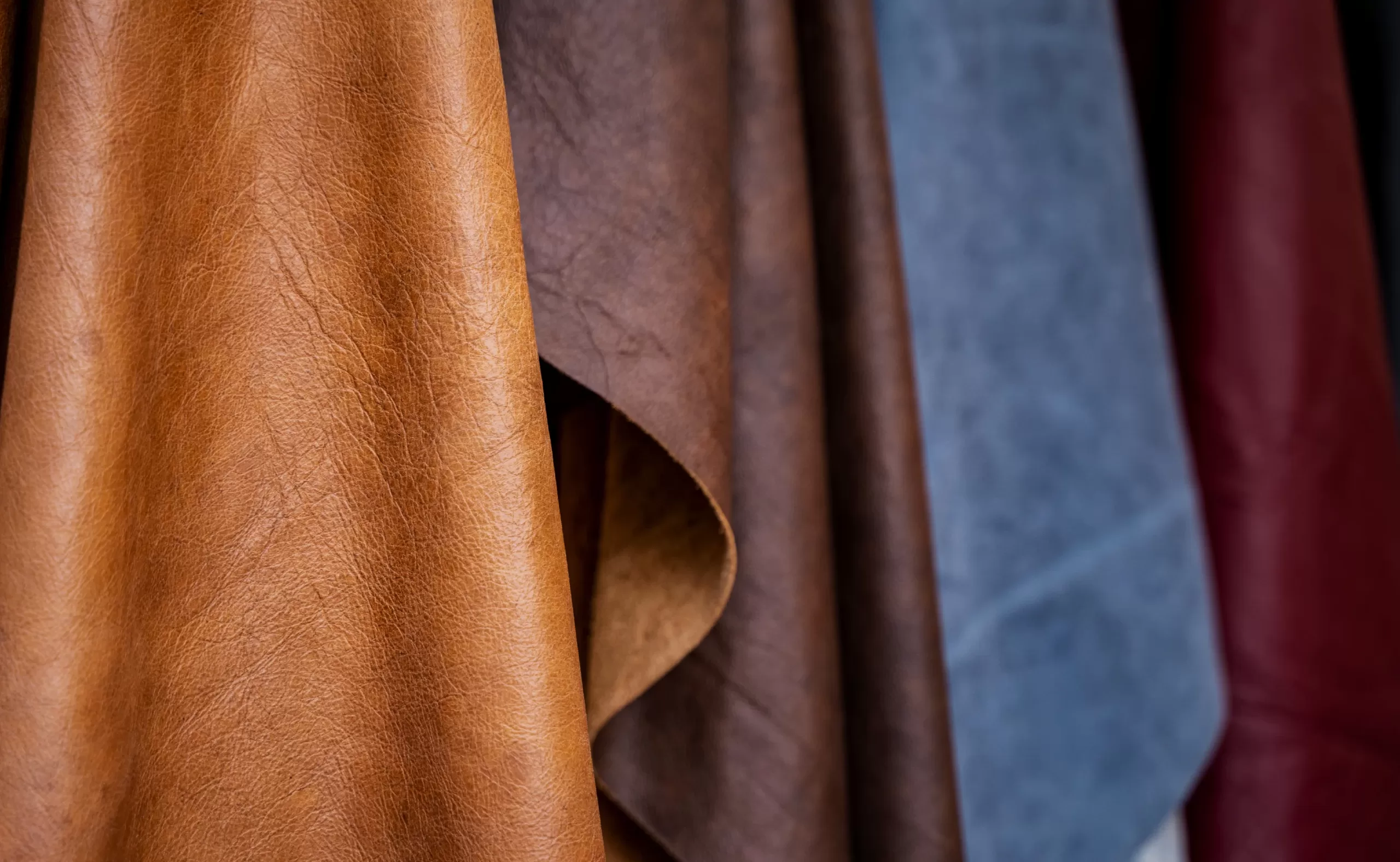 a variety of natural calf skin leathers in brown, dark brown, blue, and maroon hanging in a custom boot design workshop ready for customizations