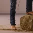 a male celebrity wears cowboy boots and dark blue jeans with one foot on the ground and one foot on a hay bale