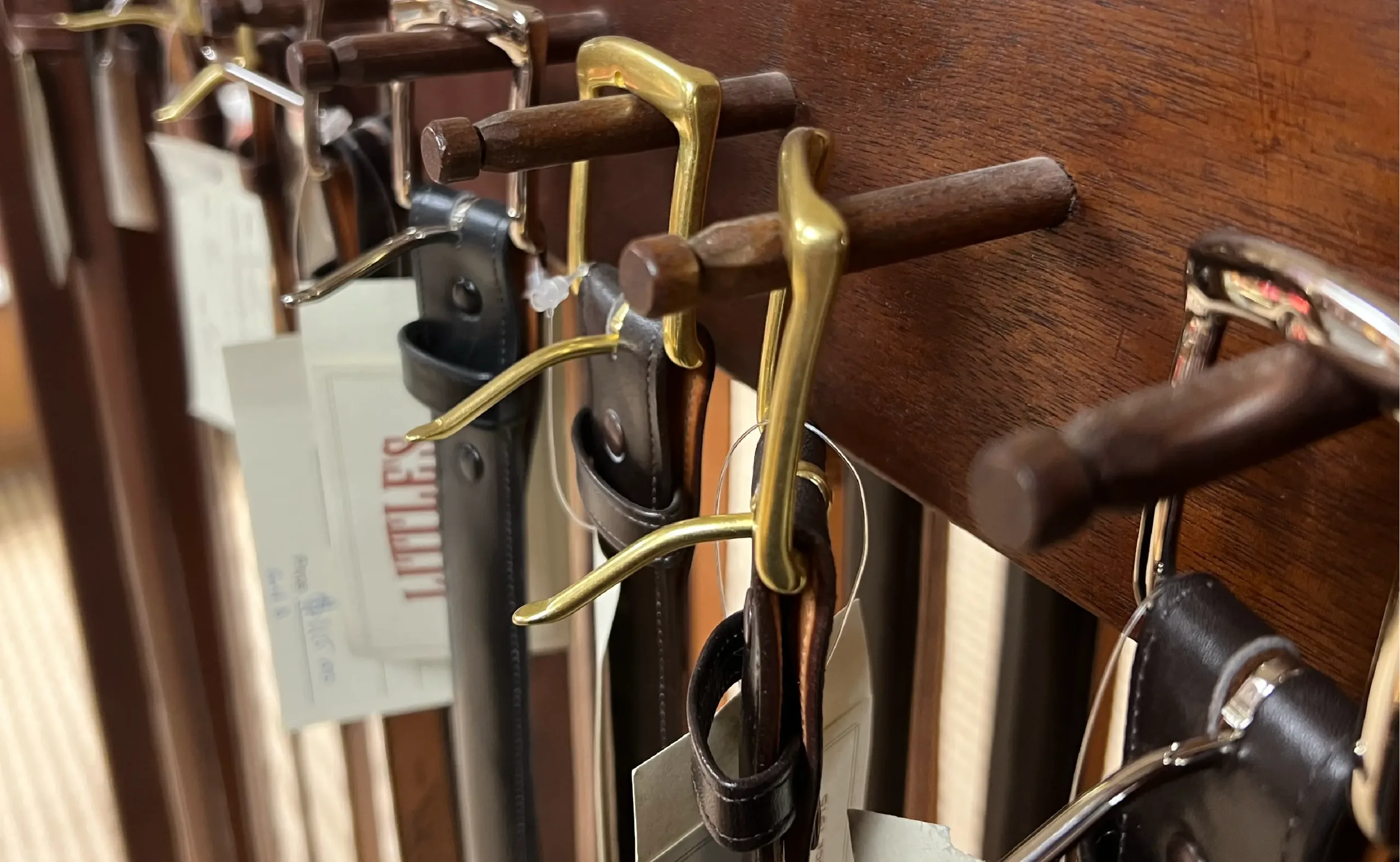 Close-up of leather belts with brass and silver buckles hanging on a wooden display rack in a Western wear store.