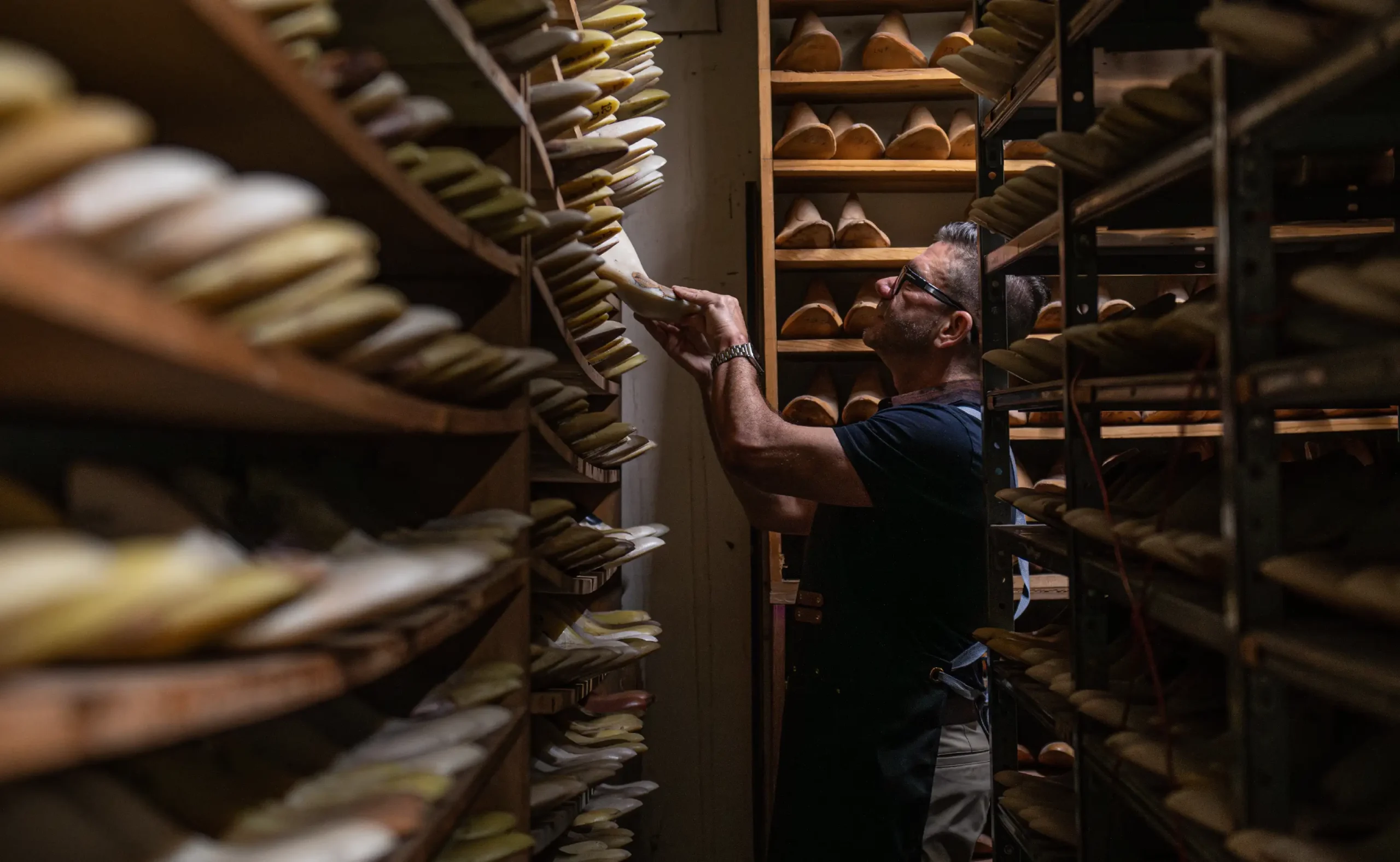 Man selects shoe form in a room lined with shelves containing many shoe forms.